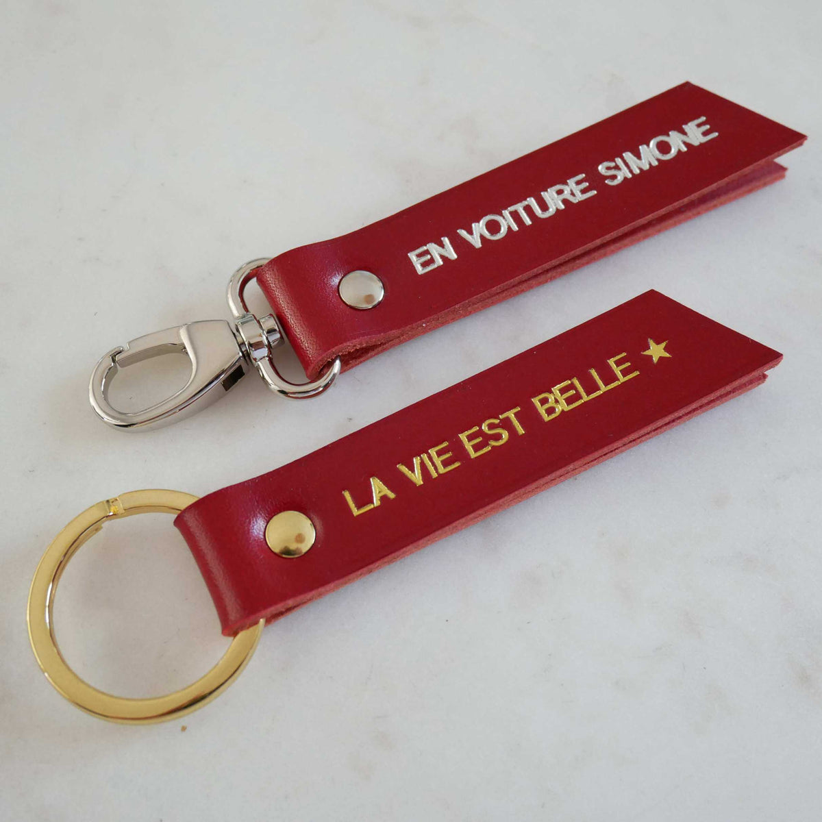 Deux porte-clés Atelier Guillocher en cuir rouge avec marquage personnalisé doré et argenté sur fond blanc